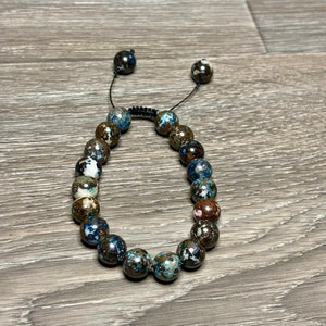 May include: A brown, blue, and white beaded bracelet with a black cord closure.