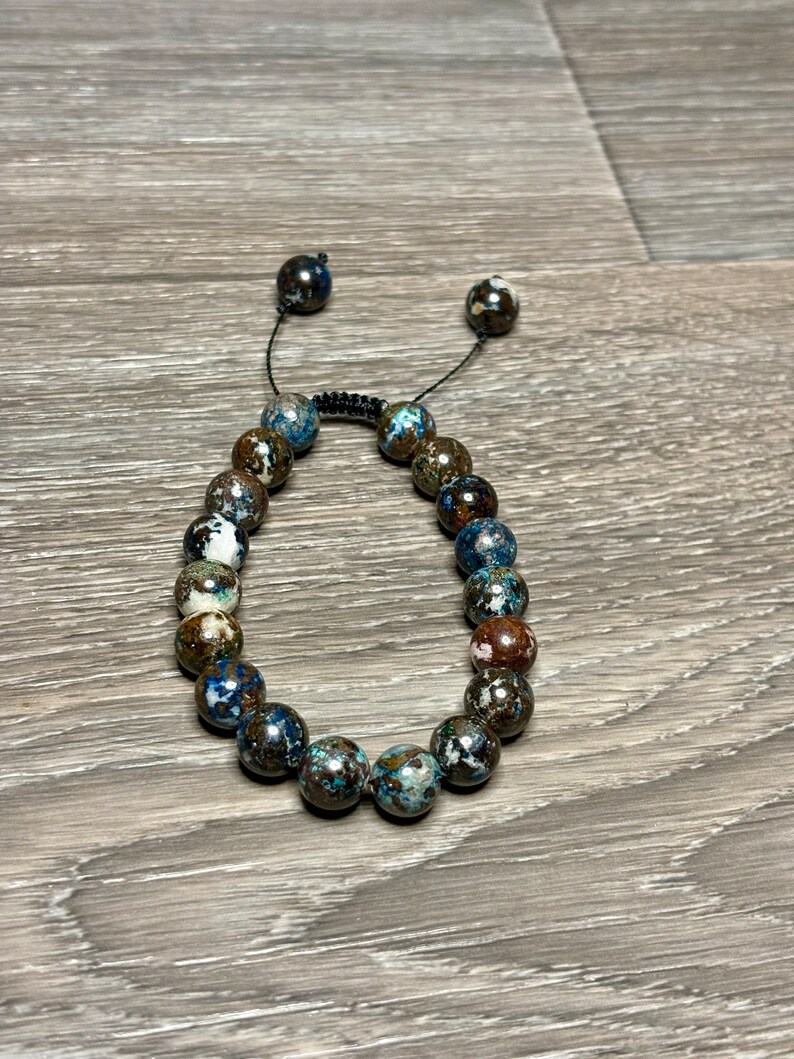 May include: A brown, blue, and white beaded bracelet with a black cord closure.