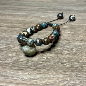 May include: A blue and brown beaded bracelet with a large, round, green and white bead as a focal point. The bracelet is tied with a black cord.