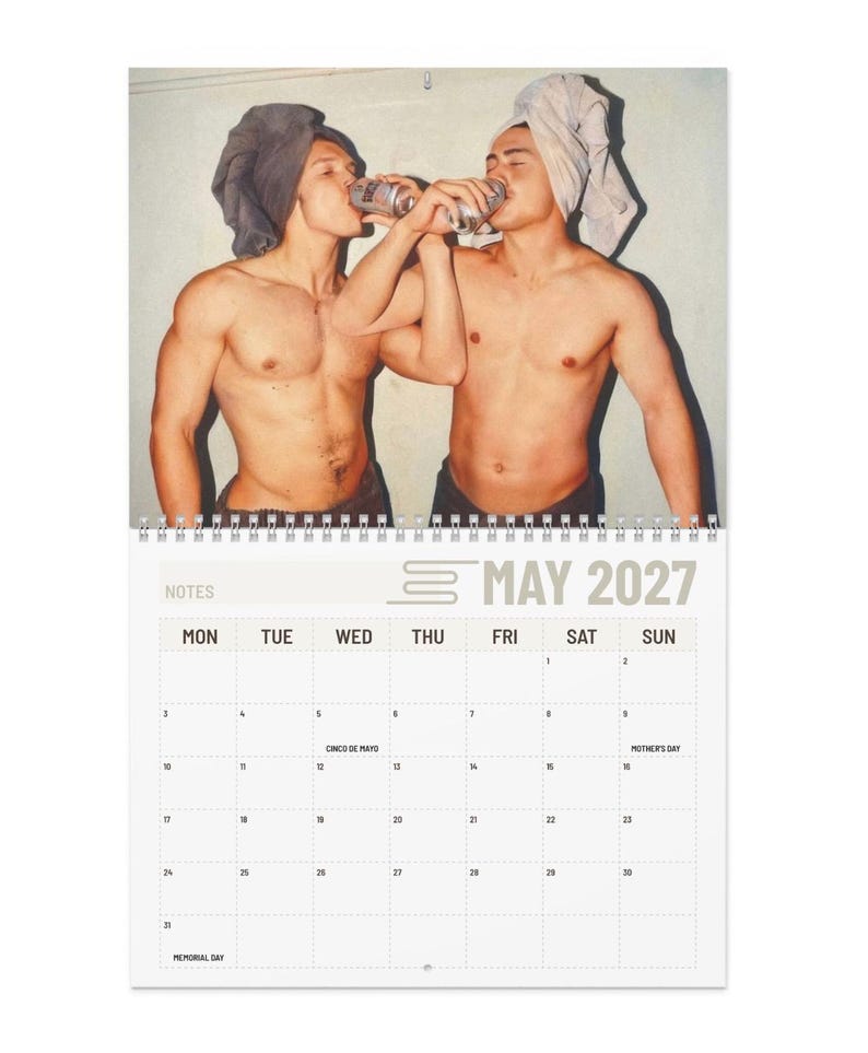Op de afbeelding: Een wandkalender voor mei 2027 met een foto van twee personen met ontbloot bovenlijf en handdoeken om hun hoofd, die elk uit een zilverkleurig blikje drinken. Het kalenderrooster bevat de tekst May 2027 en de aanduiding Notes.