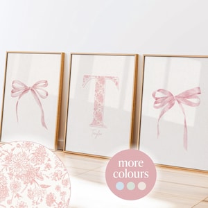 Op de afbeelding: Drie ingelijste prints met een roze bloemenontwerp. De middelste print heeft de letter "T" met de naam "Taylor" eronder. De prints staan op een lichte houten vloer.