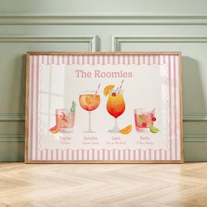 May include: A framed horizontal print titled The Roomies featuring four illustrated cocktails with names Taylor, Amelia, Lara, and Bella underneath. The design includes pink and white vertical stripes and colorful fruit garnishes on each glass.