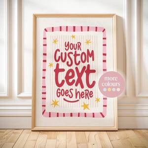 May include: A vertical rectangular framed print featuring a cream-colored background with thin vertical stripes. The text 'YOUR CUSTOM text GOES here' is written in a bold red script font, surrounded by small yellow stars and a pink striped border.