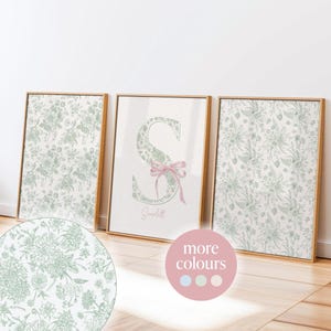 May include: Three framed art prints with floral patterns and a personalized initial. The central print features a large, floral-patterned letter "S" with a pink bow and the name "Scarlett" below. The other two prints display coordinating floral designs in green and white.