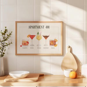 May include: A framed horizontal print titled APARTMENT 401 featuring five illustrated cocktails labeled Camryn, Keira, Tatum, Hannah, and Emma. The artwork displays various glassware including coupes and tumblers with garnishes like cherries and citrus.