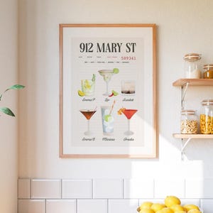 Op de afbeelding: Een ingelijste print met een lijst van cocktails met namen. De print heeft het adres "912 MARY ST" bovenaan. De cocktails omvatten een margarita, een martini en andere mixdranken, elk met een naam eronder.