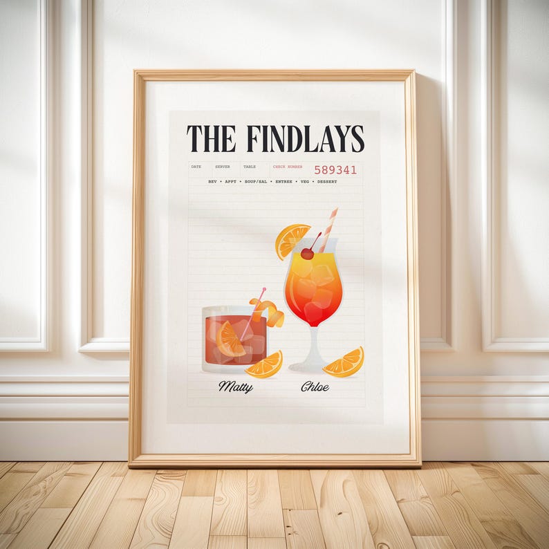 Op de afbeelding: Een ingelijste print met illustraties van twee cocktails, &eacute;&eacute;n in een tumbler en de andere in een wijnglas, gegarneerd met sinaasappelschijfjes en kersen. De print toont de tekst "THE FINDLAYS" en de namen "Matty" en "Chloe".