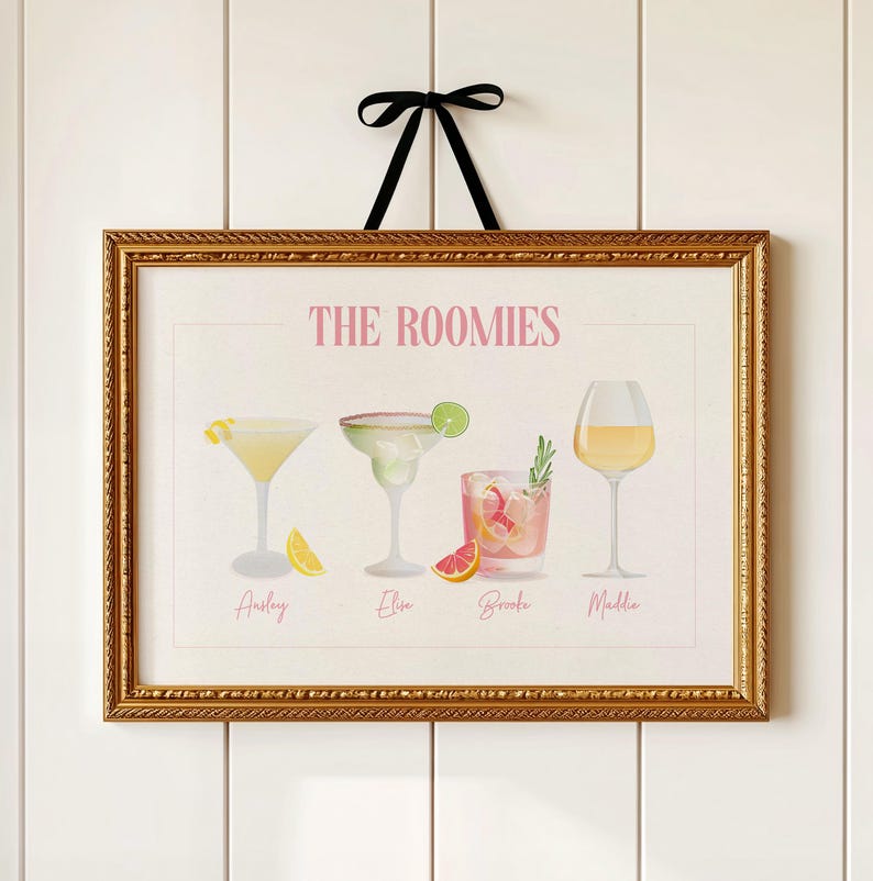 May include: A rectangular wall art print in a gold ornate frame with a black ribbon hanger. The print features the text THE ROOMIES above four cocktail illustrations with the names Ansley, Elise, Brooke, and Maddie printed below each glass.