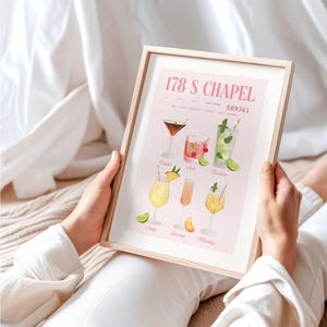 Op de afbeelding: Een ingelijste print met aquarel illustraties van cocktails. De print heeft een lichtroze achtergrond met de tekst "178 S CHAPEL" en "589341" bovenaan. Hieronder staan zes cocktail illustraties met namen als "Nadia" en "Marley".