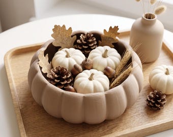 May include: A matte beige pumpkin-shaped ceramic bowl filled with three small white pumpkins, brown pinecones, acorns, dried oak leaves, and wheat stalks. A matching beige vase with dried grass and an extra white pumpkin sit nearby.