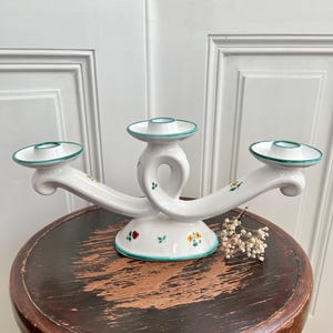 May include: White ceramic three-arm candelabra with green trim and floral details. Each arm has a circular candle holder.