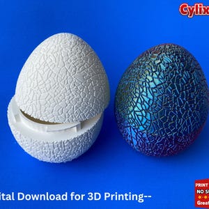 Puede incluir: Dos huevos impresos en 3D, uno blanco y otro azul con textura agrietada. El huevo blanco está abierto para revelar un interior vacío. El texto "--Descarga digital para impresión 3D--" está en la parte inferior de la imagen.