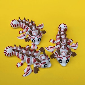 May include: Three whimsical, baseball-themed creatures with white bodies, red stitching, and brown appendages. Each has a series of miniature baseballs along its back and head, with black eyes. The background is a solid yellow.