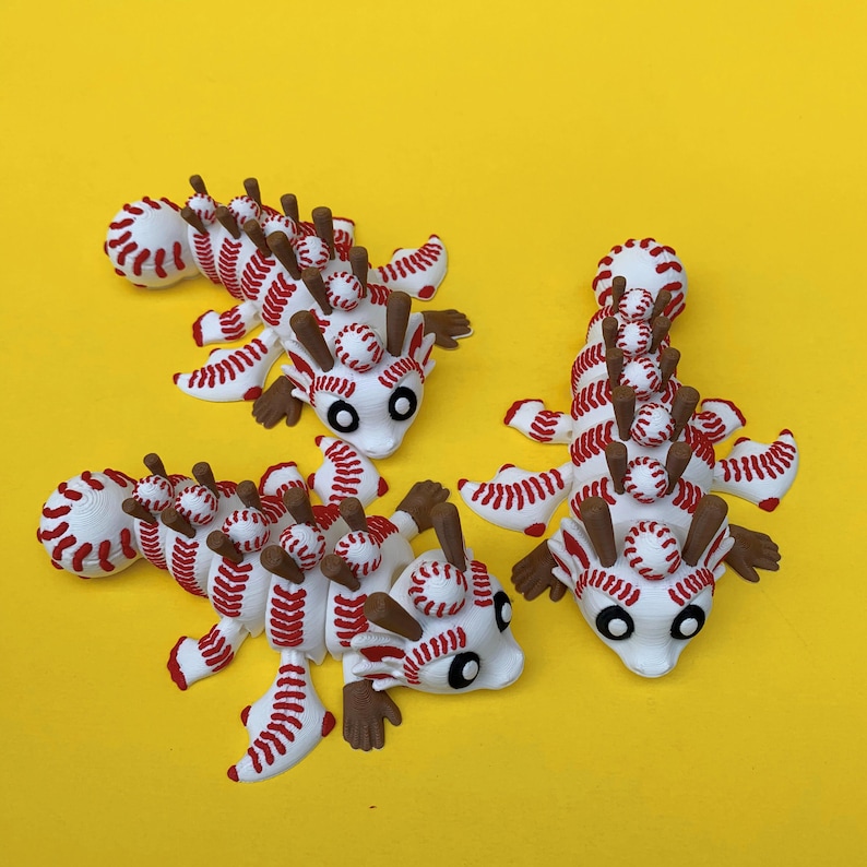 May include: Three whimsical, baseball-themed creatures with white bodies, red stitching, and brown appendages. Each has a series of miniature baseballs along its back and head, with black eyes. The background is a solid yellow.