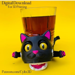 Puede incluir: Un soporte negro con forma de gato impreso en 3D con detalles en rosa, sosteniendo un vaso de líquido ámbar. El gato tiene ojos amarillos y nariz y boca rosas. El texto en la imagen dice "Digital Download For 3D Printing" y "Patreon.com/Cylix3D".