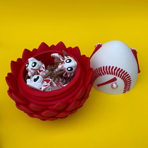 May include: A red, flower-shaped container holds several white and red baseball-themed figurines. A baseball-shaped container is open next to the flower. The background is a solid yellow.
