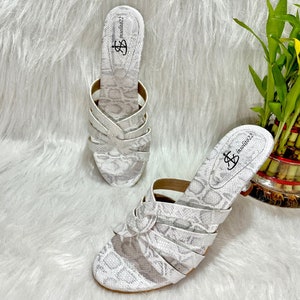 May include: A pair of white and gray snake-print sandals. The sandals have multiple straps and a knotted detail on the front. The insole has the text "insolito22" printed on it.