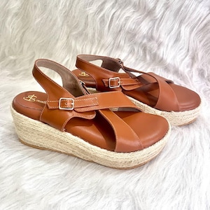 May include: A pair of brown leather sandals with a woven jute platform sole. The sandals feature adjustable straps with silver buckles. The platform sole is approximately 2 inches high.
