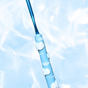 May include: A blue ceramic crochet hook with a white cloud design and a rainbow charm. Bisou Ceramics.