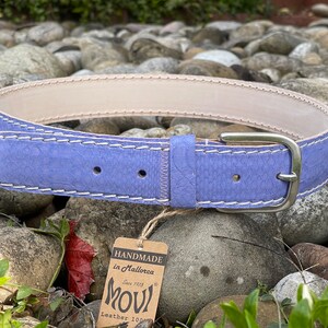 Könnte beinhalten: Ein hellvioletter Ledergürtel mit weißen Nähten und einer silbernen Schnalle. Der Gürtel ist handgefertigt in Mallorca, Spanien, und besteht aus 100% Leder.