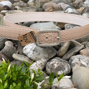 Könnte beinhalten: Ein hellrosa Schlangenledergürtel mit einer silbernen Schnalle. Der Gürtel ist handgefertigt in Italien und hat ein Etikett mit der Aufschrift "Handmade in Italia" und "Movi Leather 100%".