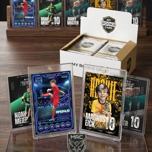 May include: A collection of My Rookie Card trading cards displayed in clear plastic cases and a cardboard box. The cards feature young athletes in sports uniforms with text including names like Magnus Eick and Noah Meier, plus stats and logos.