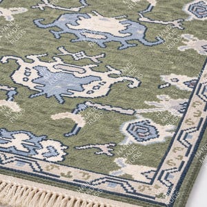 May include: Green rectangular rug with a detailed pattern in blue and off-white. The rug has a fringe on one end and the words "HAND MADE RUGS" are printed on the rug.