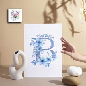 May include: A watercolor print of the letter B surrounded by blue flowers. The print is on white paper and has a white border.
