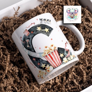 May include: White ceramic mug with a watercolor illustration of a movie theme. The mug features a large letter "C" with a film reel, popcorn, and stars. The text "Cinematic Art" is visible in the background.