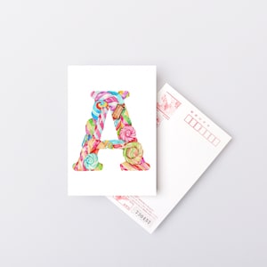 K&ouml;nnte beinhalten: Eine Postkarte mit einer Aquarell-Illustration des Buchstabens A, der aus bunten S&uuml;&szlig;igkeiten besteht. Der Buchstabe ist von einem wei&szlig;en Rand umgeben.