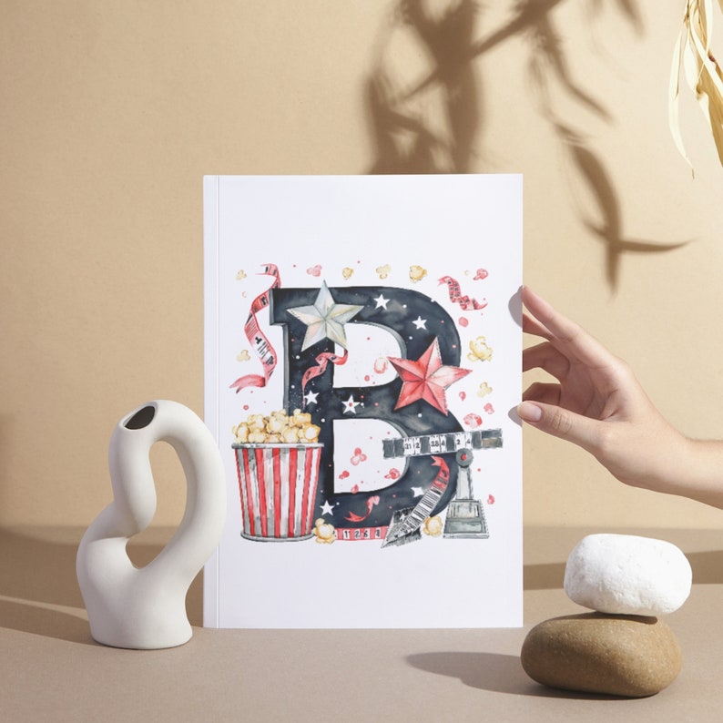 May include: A watercolor illustration of the letter B decorated with movie-themed elements, including popcorn, a film reel, and stars. The letter is black with white stars and red accents.