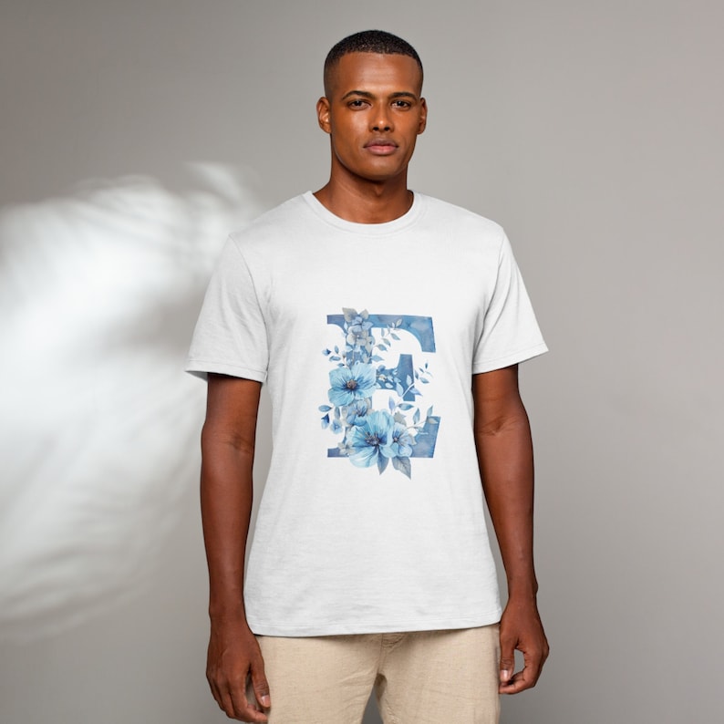 May include: White t-shirt with a blue watercolor floral design featuring the letter "E".