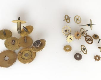 May include: A collection of vintage watch gears in various sizes and shapes, made of brass and other metals. The gears are arranged on a white surface, showcasing their intricate designs and aged appearance.