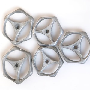 Puede incluir: Cinco pomos hexagonales de metal plateado con tres agujeros cada uno. Los pomos tienen una superficie lisa y ligeramente texturizada.