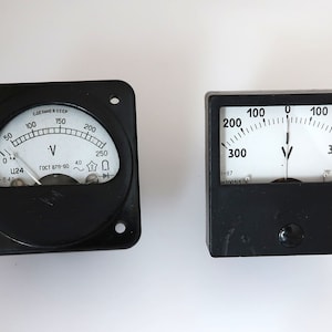 Puede incluir: Dos voltímetros analógicos con cajas negras y caras blancas. El voltímetro de la izquierda tiene un rango de 0 a 250 voltios y el voltímetro de la derecha tiene un rango de 0 a 300 voltios. Ambos voltímetros tienen una aguja que apunta a cero.