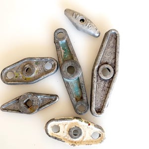 May include: A collection of vintage metal hardware pieces in various shapes and sizes. The pieces are primarily silver with hints of green and white paint, showing signs of wear. Some pieces have holes and a central circular opening.
