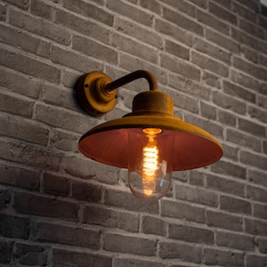 May include: A yellow metal wall sconce with a red-brown shade and a clear glass bulb. The sconce is mounted on a brick wall.