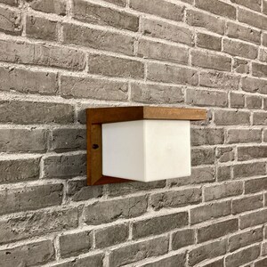May include: A white square light fixture with a wooden frame mounted on a brick wall.
