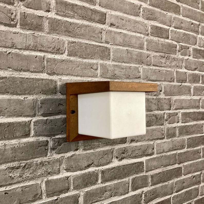 May include: A white square light fixture with a wooden frame mounted on a brick wall.