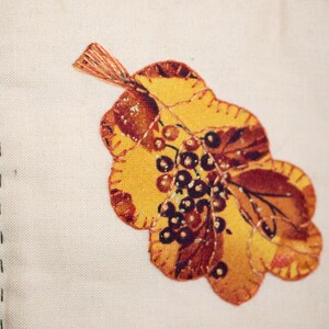 May include: An embroidered leaf in yellow and brown with a cluster of small brown berries in the centre.