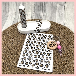 Könnte beinhalten: Ein Set mit leopardengemusterten Artikeln, darunter eine Kerze, ein Tablett, ein Aufkleberbogen und ein Schlüsselanhänger mit rosa Perlen.