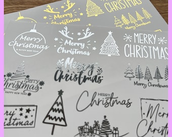 Op de afbeelding: Een vel met zilveren en gouden kerst stickers met verschillende ontwerpen, waaronder kerstboom, rendier, sterren en de woorden "Merry Christmas".