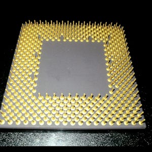 Peut inclure: Gros plan sur un processeur d'ordinateur. Il présente un corps carré gris et de nombreuses broches dorées disposées sur le pourtour. Les broches sont espacées uniformément et dressées. Le fond est noir, mettant en valeur le design.