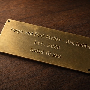 Puede incluir: Una placa rectangular de latón macizo con esquinas redondeadas y cuatro pequeños orificios de montaje. La superficie está grabada con el texto: Forge and Font Atelier - Den Helder, Est. 2026, Solid Brass. El metal tiene un acabado mate cepillado.