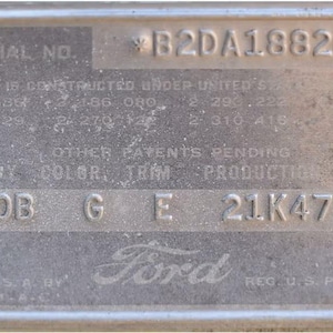 May include: A rectangular silver-toned metal Ford vehicle identification plate featuring the serial number B2DA188268, various patent numbers, and production codes 70B, G, E, and 21K477. The plate includes two screw holes and embossed text.