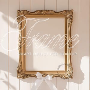 Puede incluir: Un marco de imagen dorado adornado con un fondo blanco. El marco tiene un diseño decorativo y está sentado en una pared blanca.