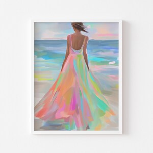 May include: A framed art print depicts a person in a flowing, colorful dress, standing on a beach and facing the ocean. The dress features shades of pink, orange, and green. The artwork is a watercolor style painting.