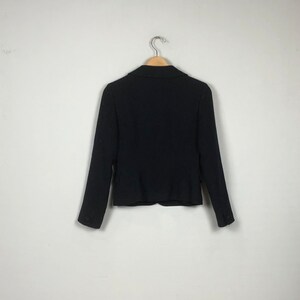 May include: A black blazer with a notched collar and long sleeves. The blazer is hanging on a wooden hanger against a white background.