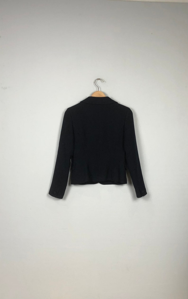 May include: A black blazer with a notched collar and long sleeves. The blazer is hanging on a wooden hanger against a white background.