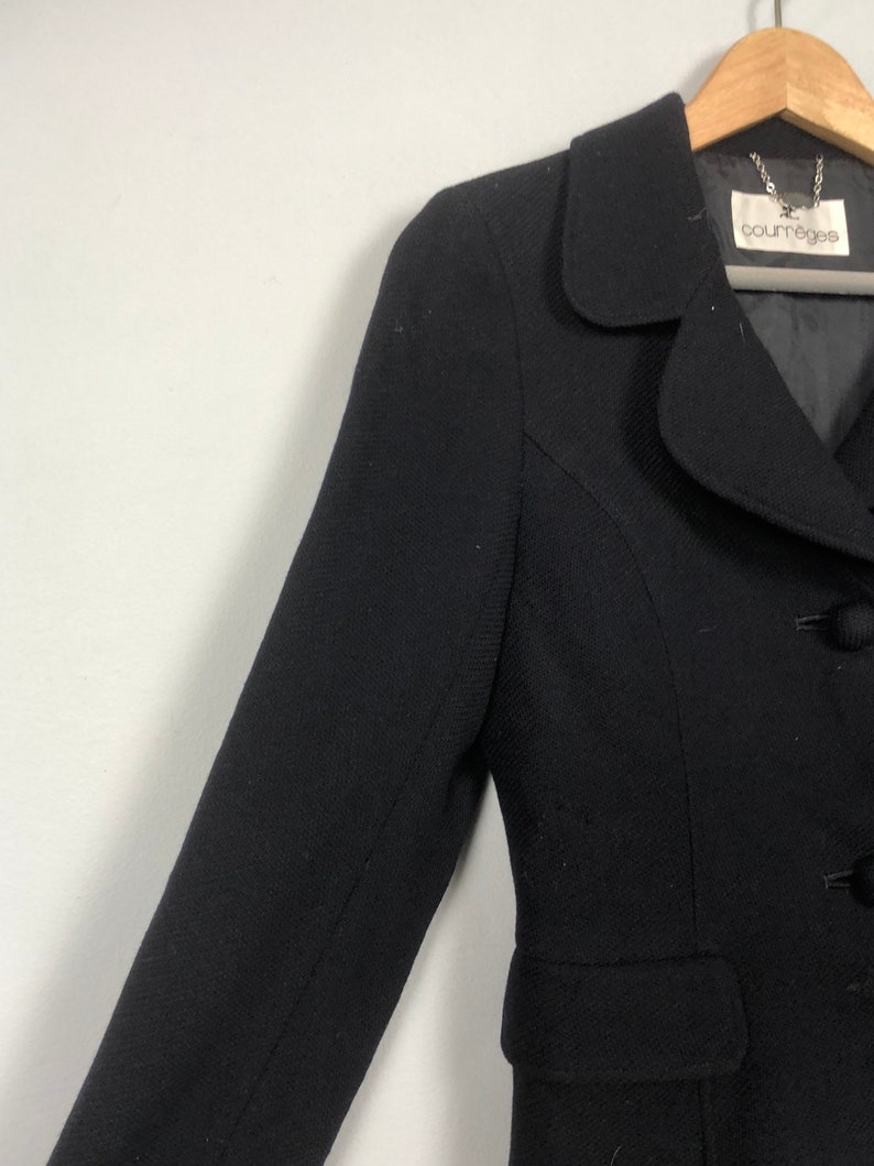 May include: A black blazer with a single button closure and a small pocket on the left side. The blazer has a small, rounded collar and the label "Courr&egrave;ges" is visible on the inside of the collar.